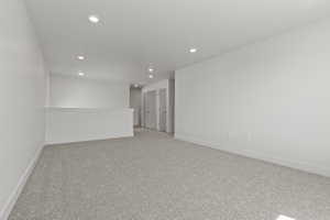 Spacious carpeted room featuring recessed lighting, light gray wall-to-wall carpeting, white baseboards, and a white interior railing