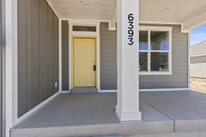 Covered front porch featuring a vibrant yellow entry door with transom window, grey siding, and a white architectural column