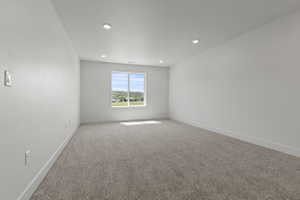 Spacious room featuring neutral carpeting, recessed ceiling lighting, a large window, white baseboards, and light-toned walls