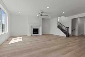 Spacious room featuring wood-finish flooring, a white mantel fireplace with a tile surround, and a ceiling fan