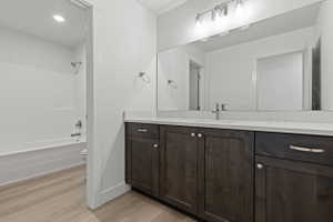Bathroom featuring wood-finish vanity cabinetry with brushed nickel hardware, a white countertop, a wide mirror, and a white tub-shower combination