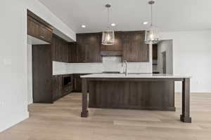 Kitchen featuring dark wood cabinetry, white countertops, a tile backsplash, and light wood-finish flooring