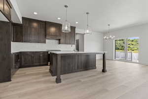 Modern kitchen featuring dark wood cabinetry, a white tile backsplash, and light wood-finish flooring