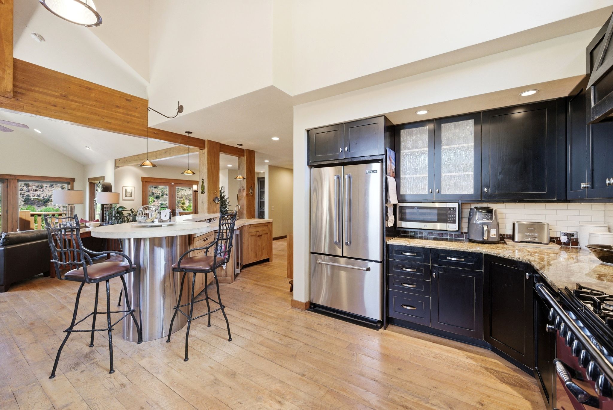 Expansive kitchen featuring wood-finish flooring, stainless steel appliances, dark cabinetry, and granite countertops