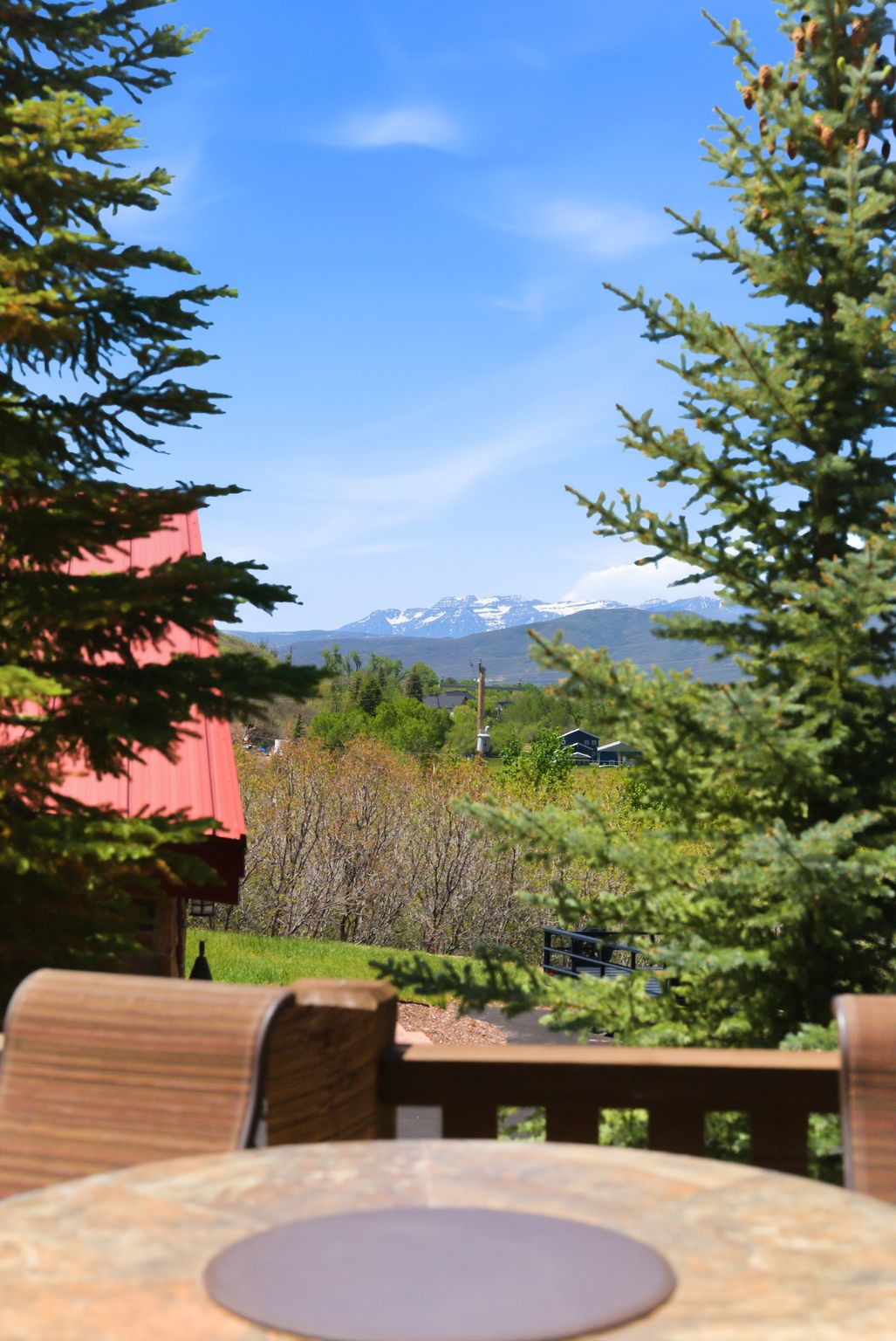 Outdoor deck area with a stone-finish table, offering distant mountain scenery and mature evergreen trees
