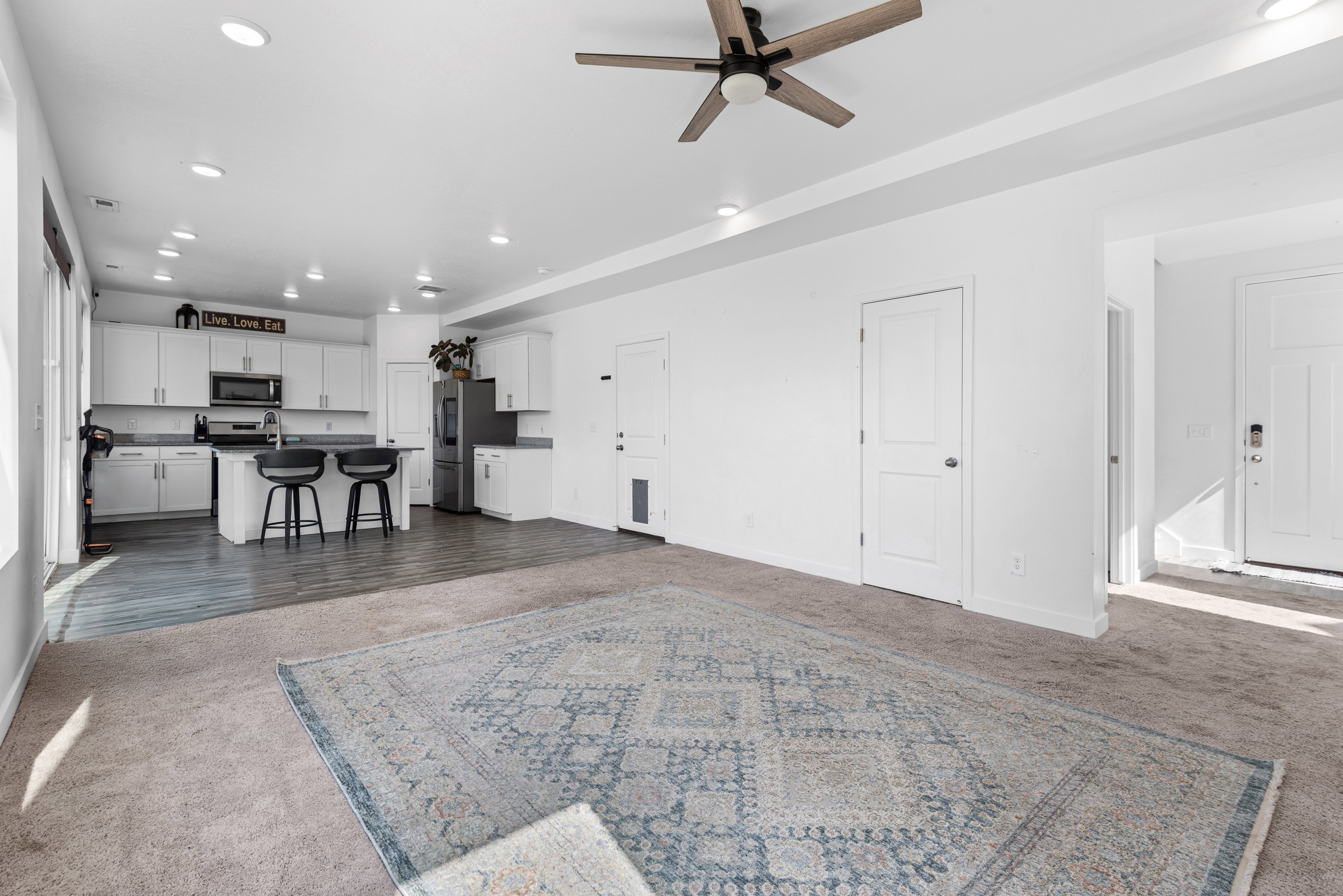 Open-concept living area featuring a modern kitchen with white cabinetry, stainless steel appliances, and an island with seating