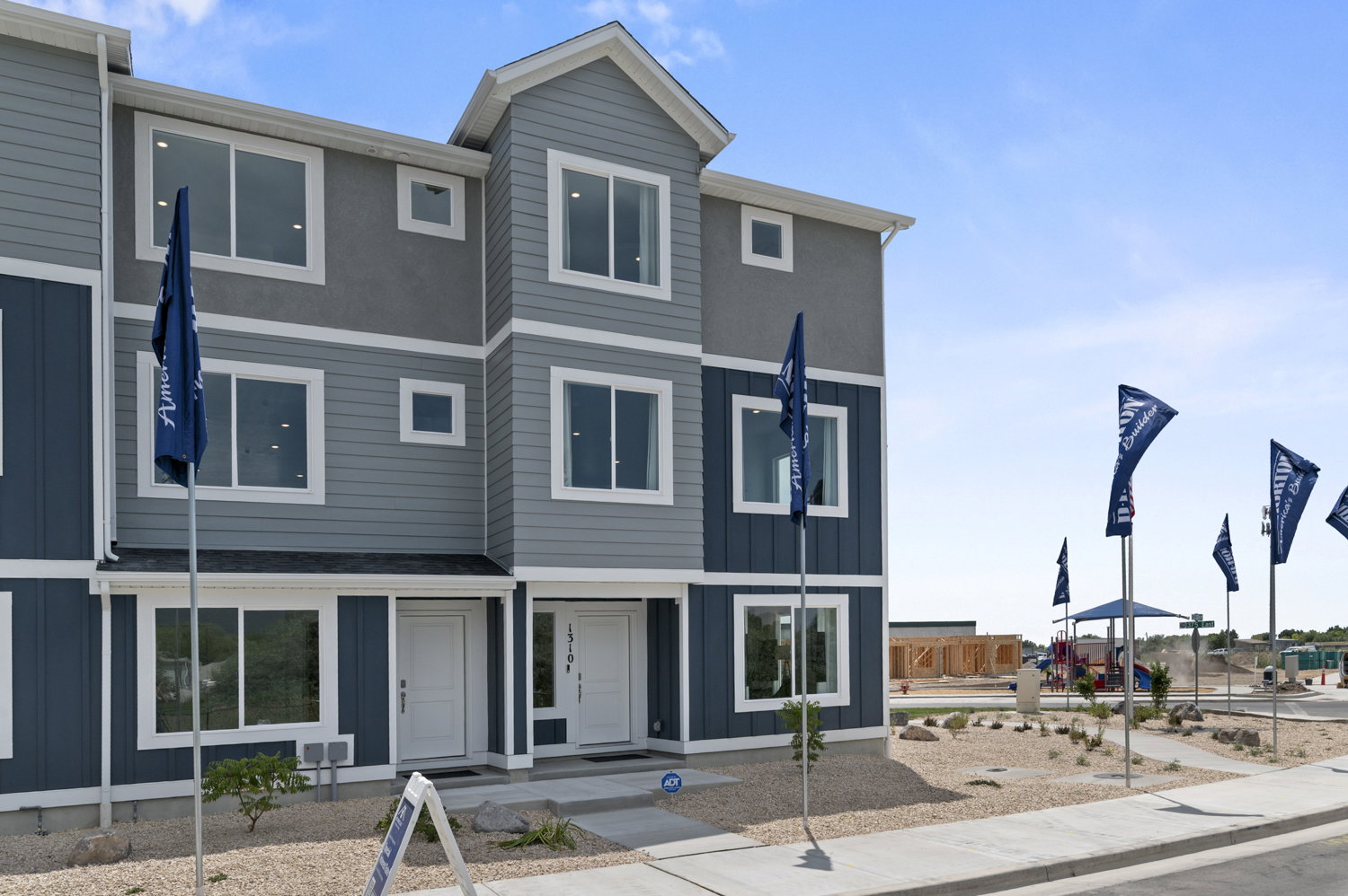 Multi-story townhome exterior featuring blue and grey siding, white trim, multiple windows, and a paved walkway
