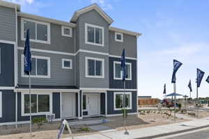 Multi-story townhome exterior featuring blue and grey siding, white trim, multiple windows, and a paved walkway