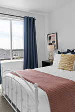 Bright bedroom featuring a large window with blue privacy drapes, a white metal bed frame, and carpeted flooring
