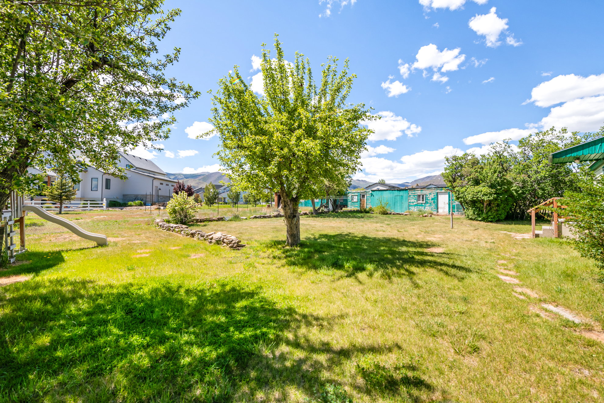 Expansive grassy yard featuring mature trees, a white picket fence, and distant mountain vistas