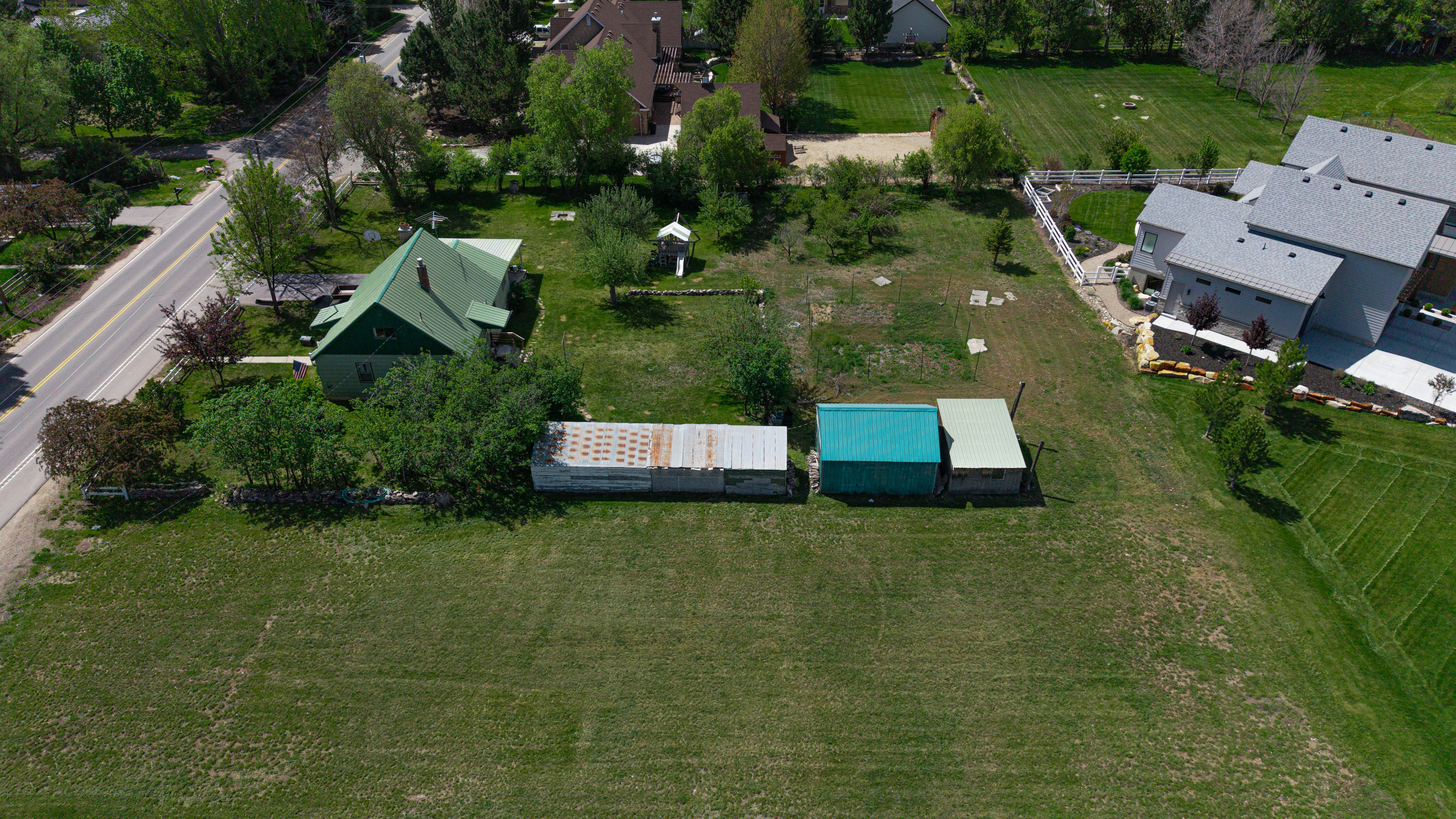 Expansive grassy lot with established trees and two outbuildings