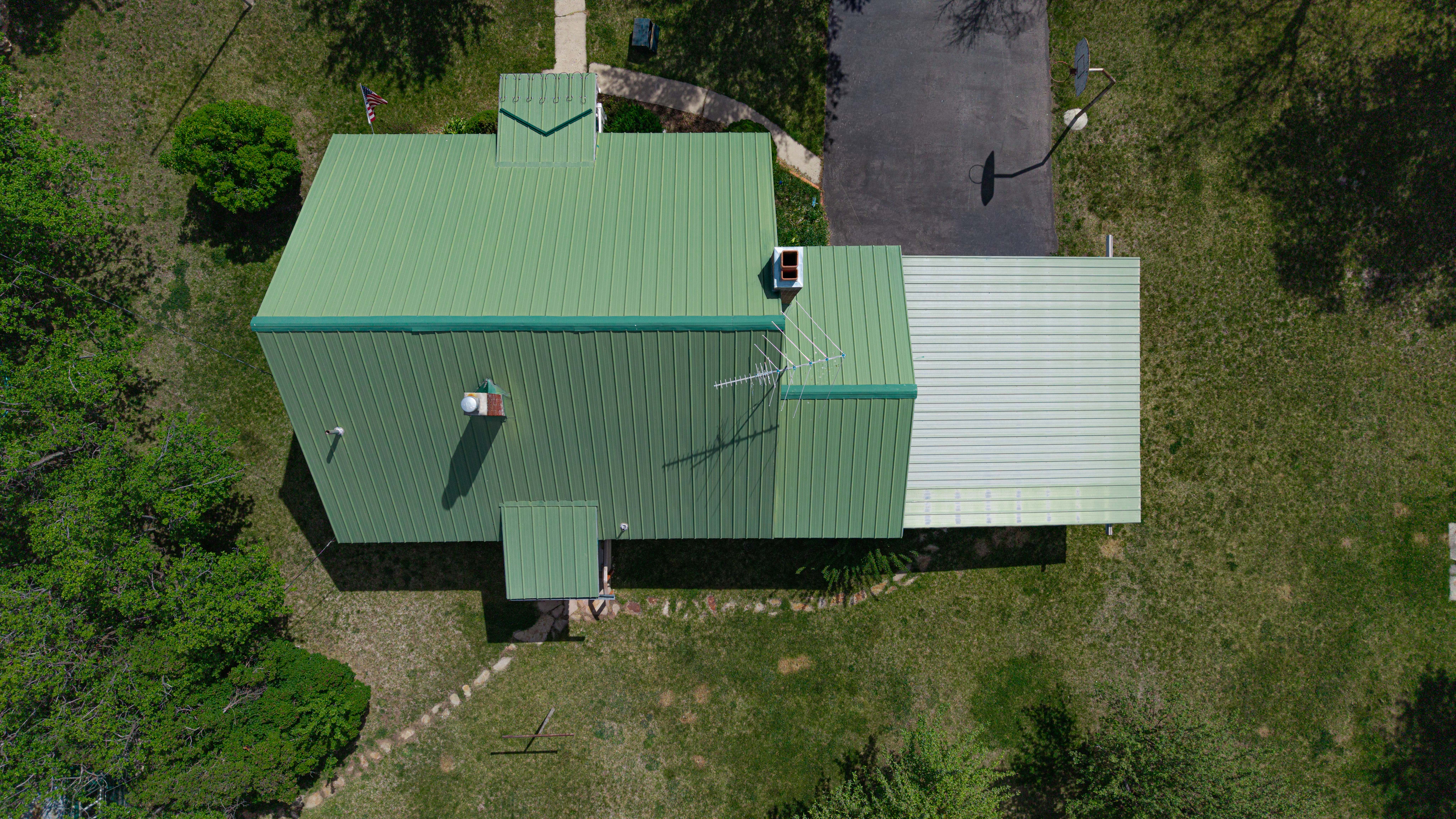 Property featuring a vibrant green metal roof, a contrasting light-colored extension roof, and a paved driveway
