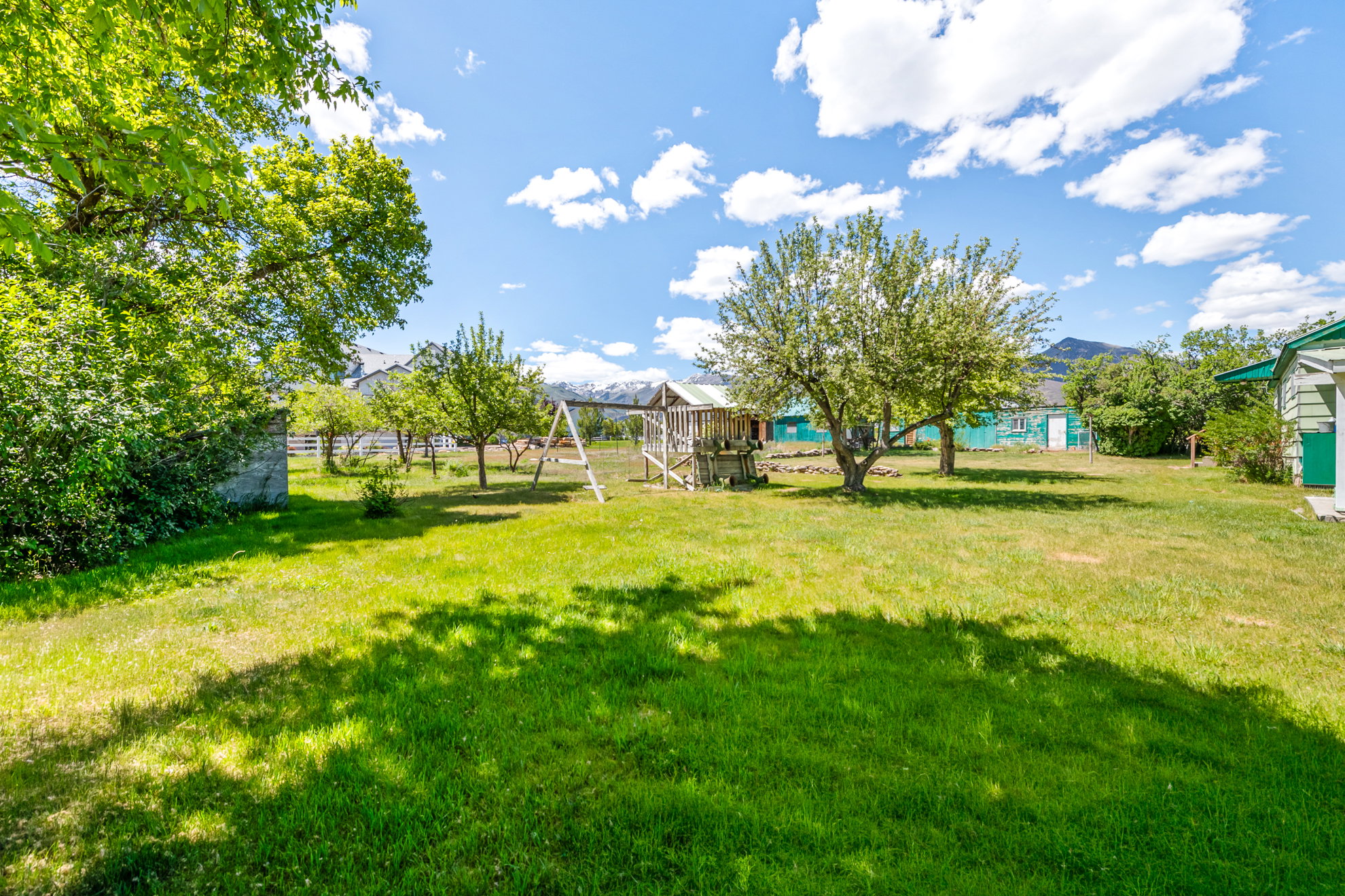 Spacious backyard featuring a manicured lawn, mature trees, and a mountain backdrop