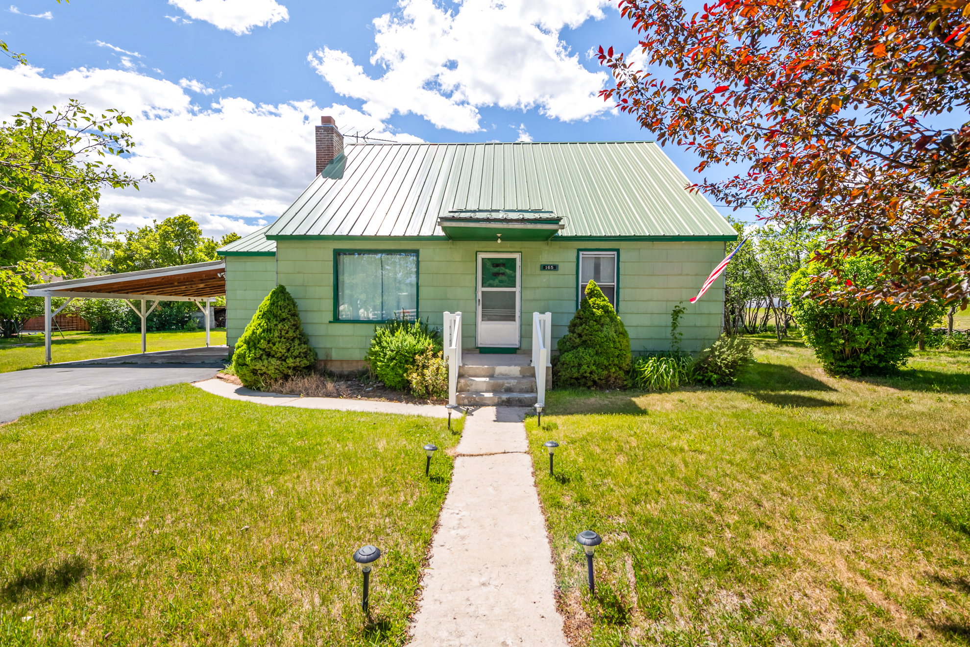 Single-story home featuring a green metal roof, light green siding, and a covered carport