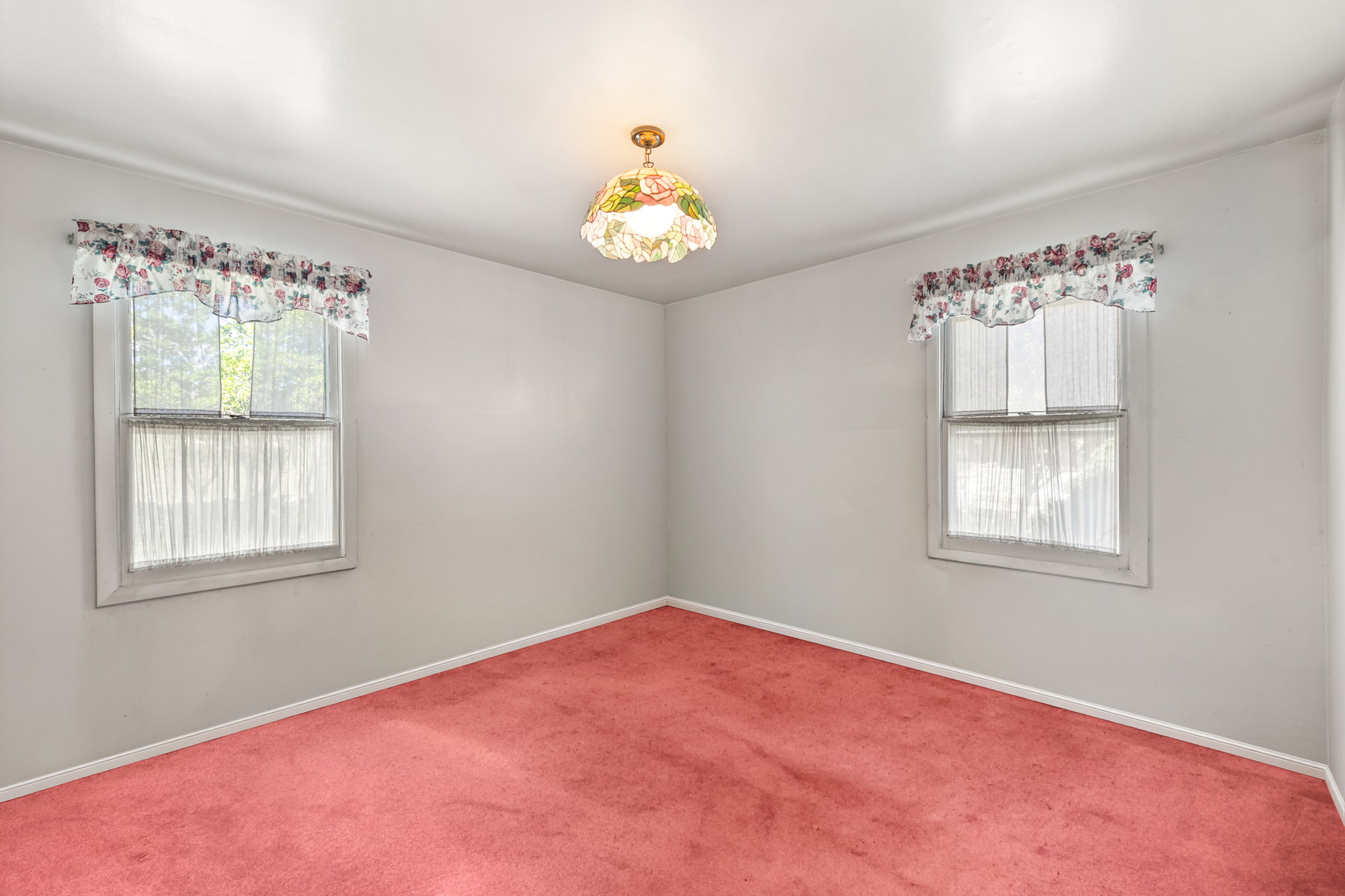 Bright room featuring twin windows, light-colored walls, red carpeting, white trim, and an overhead light fixture
