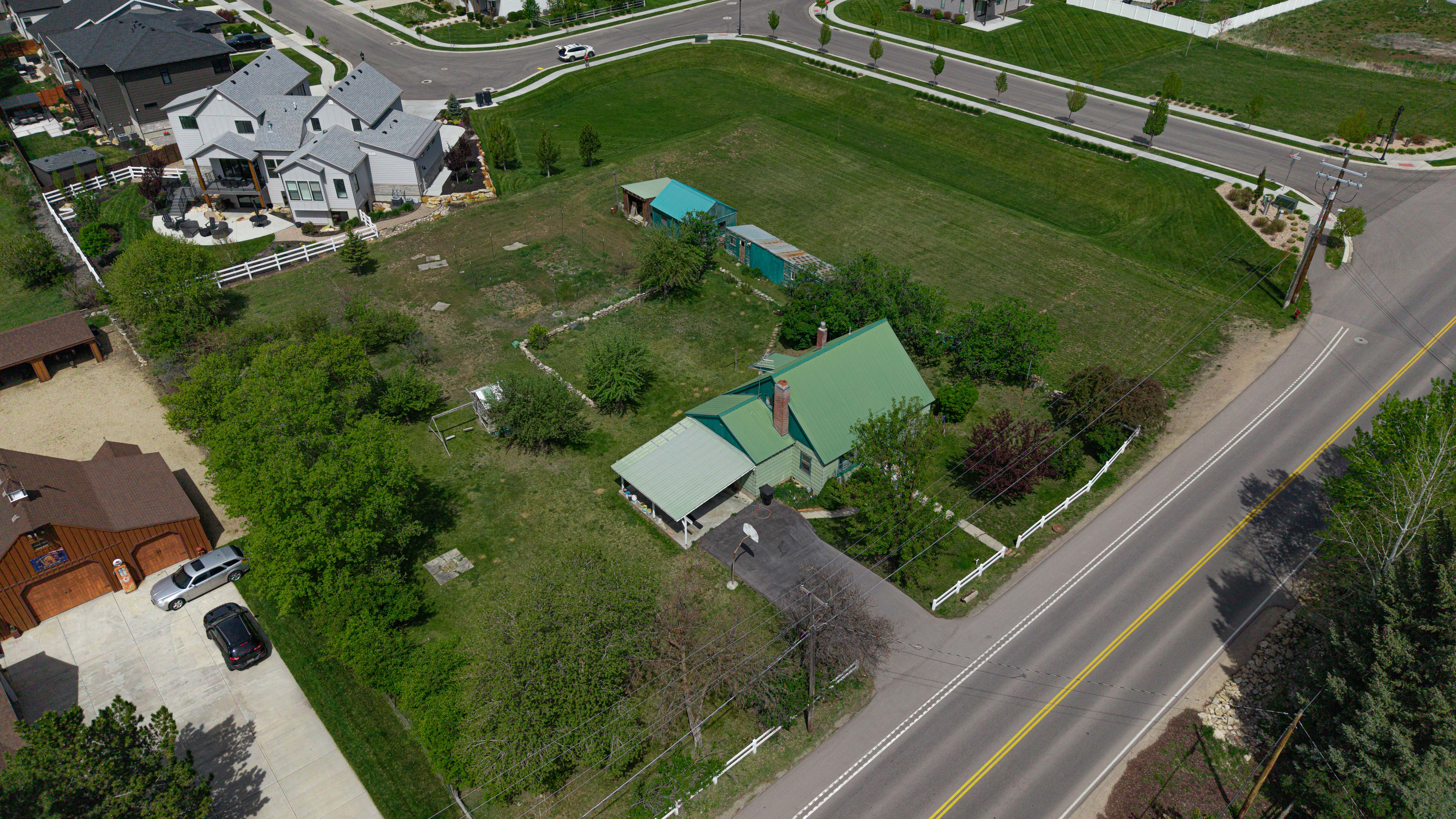 Expansive property featuring a green-roofed residence, extensive grassy areas, and mature trees