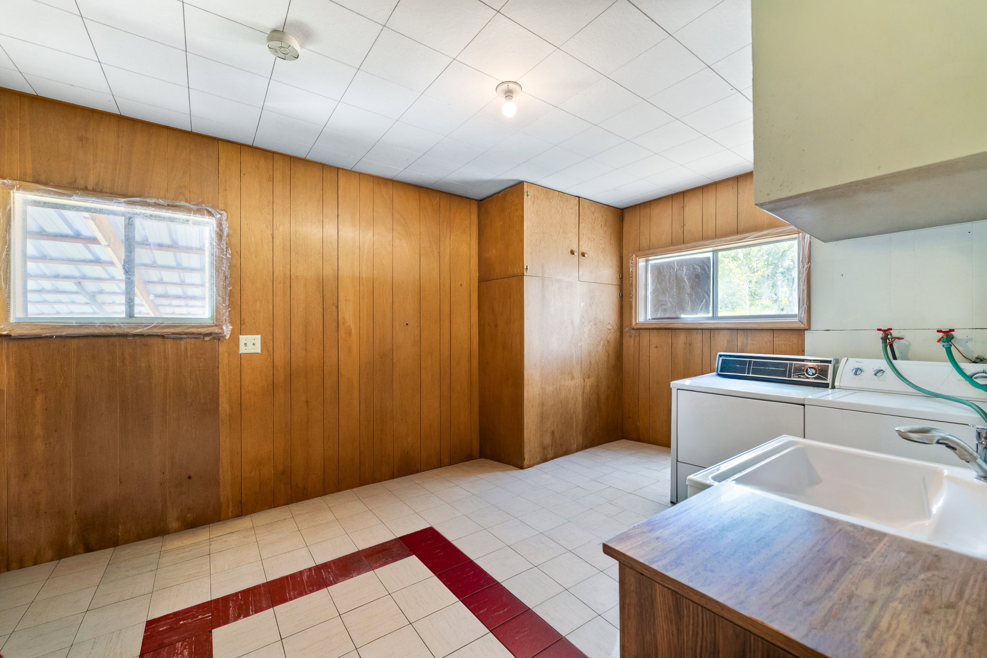 Utility room featuring wood paneling, built-in storage cabinetry, two windows, and a utility sink with a wood-finish countertop