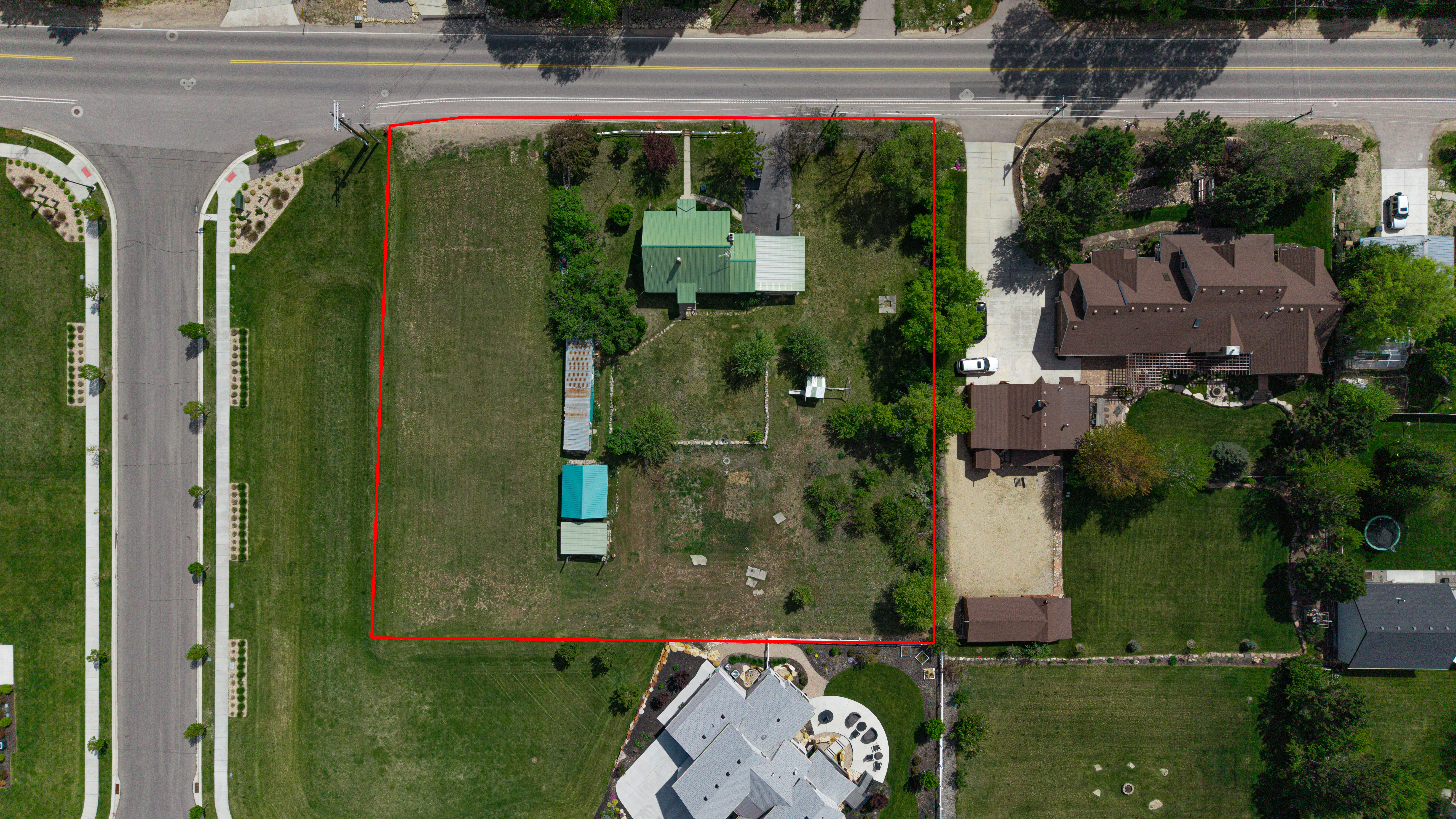 Expansive corner lot featuring a main residence with a green roof, two accessory structures, and mature trees