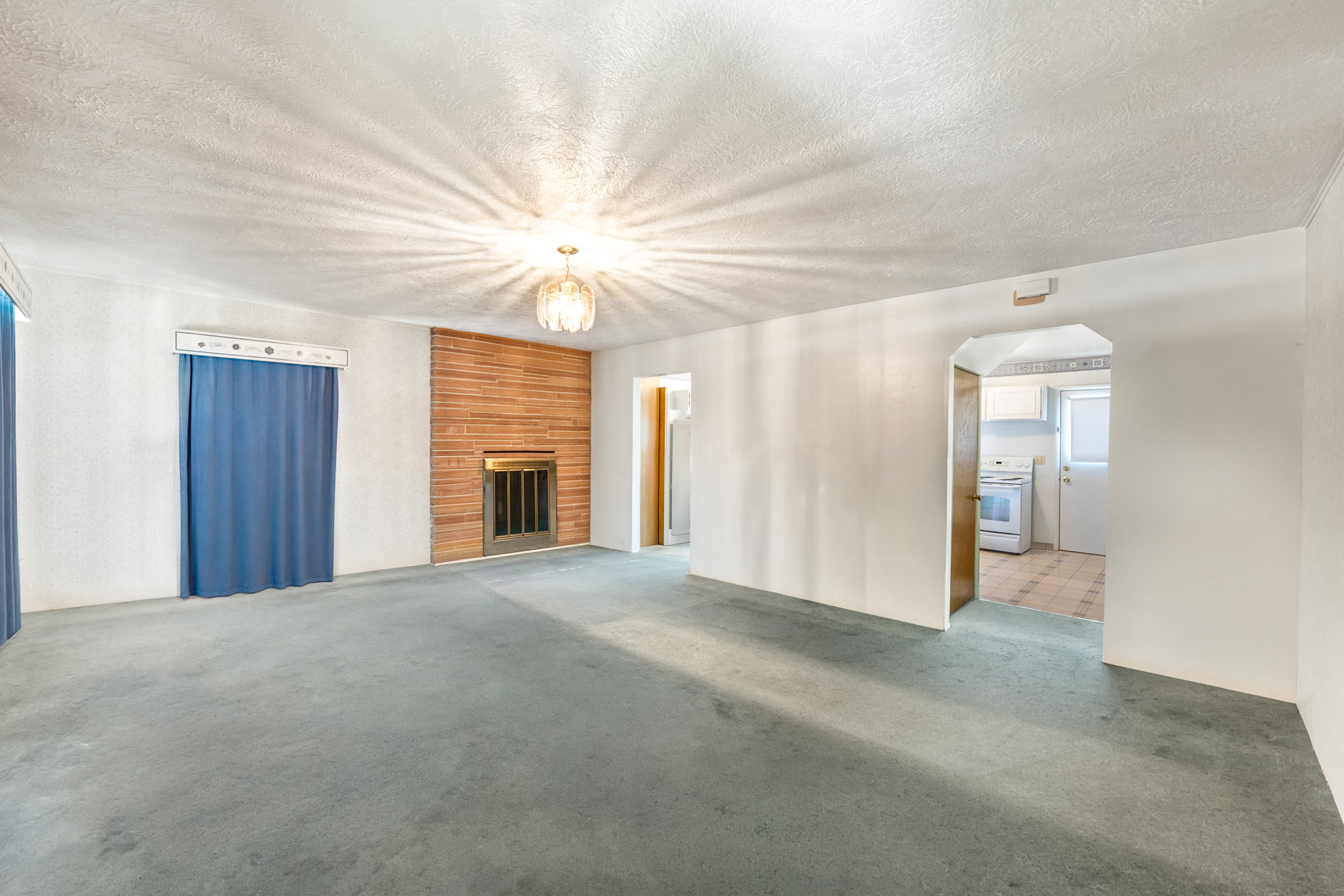 Spacious living area featuring a brick fireplace with a metal grate, textured white walls, blue window coverings, and a ceiling-mounted light fixture