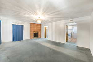 Spacious living area featuring a brick fireplace with a metal grate, textured white walls, blue window coverings, and a ceiling-mounted light fixture