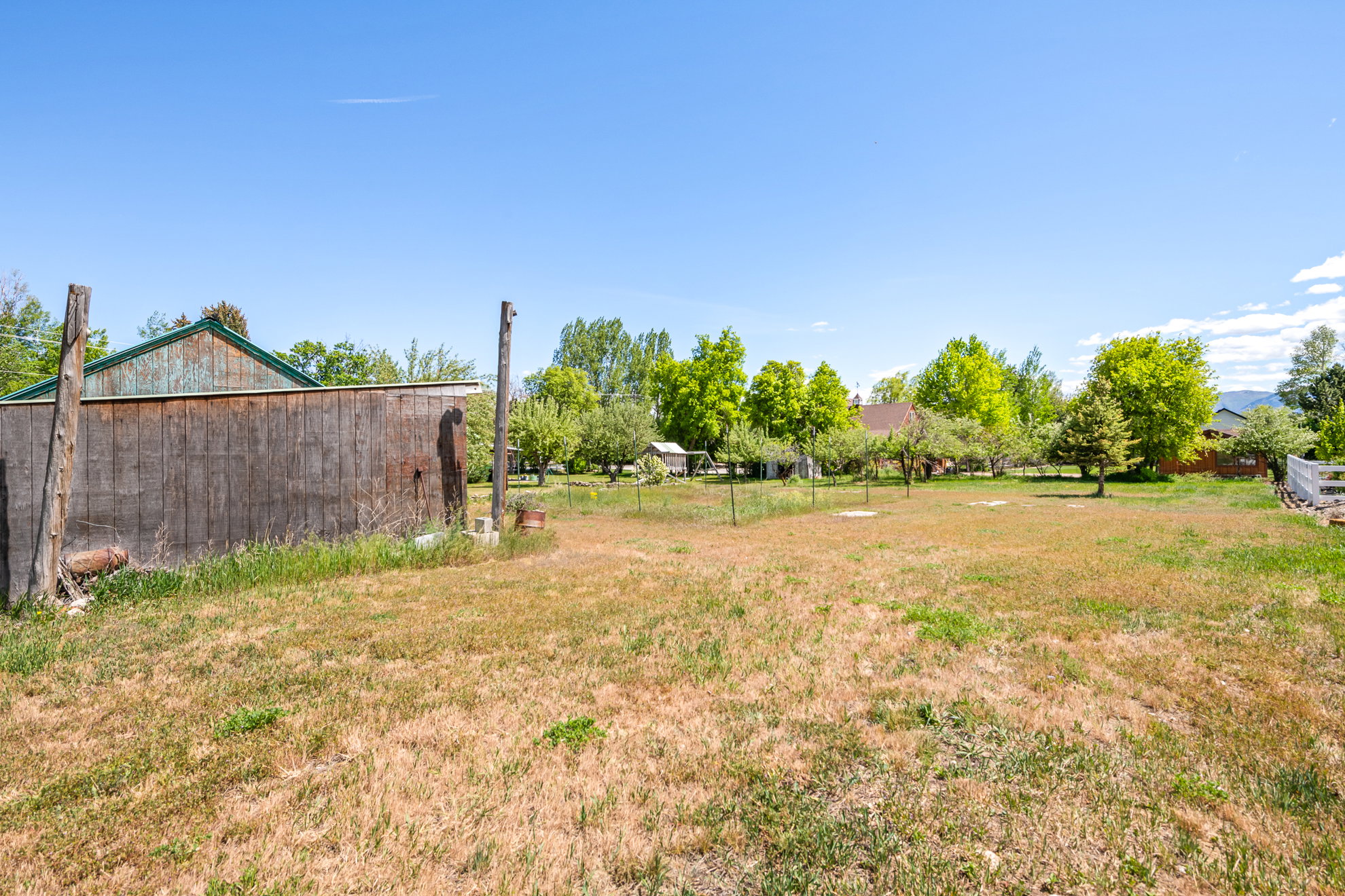 Expansive open yard space featuring a rustic wood-sided structure with a green-toned roof