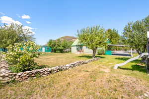 Spacious outdoor area featuring a dry-stacked stone retaining wall, mature trees, and a detached carport