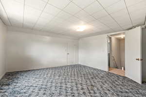Spacious room featuring textured carpeting, white painted walls, and a dropped ceiling with recessed lighting