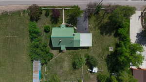 Property featuring a green metal roof, expansive green space, mature trees, and a concrete driveway