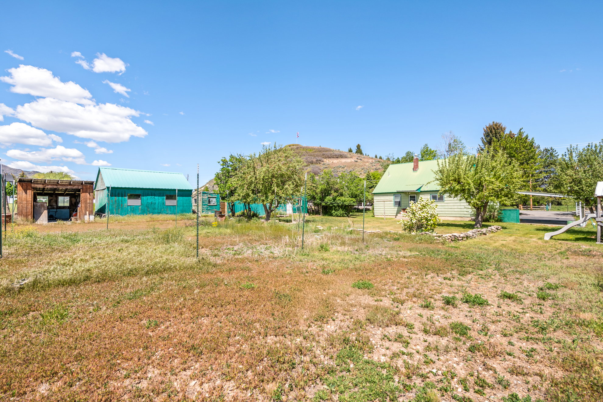Expansive property featuring multiple structures, including a green-sided building with a metal roof and a light-colored home with a green gable roof