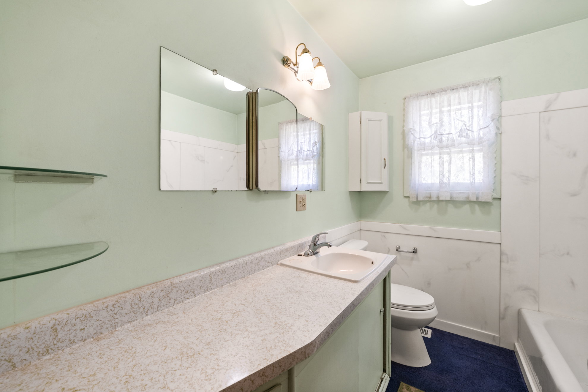 Bathroom featuring a vanity with an integrated sink, a wall-mounted mirror, and glass shelving