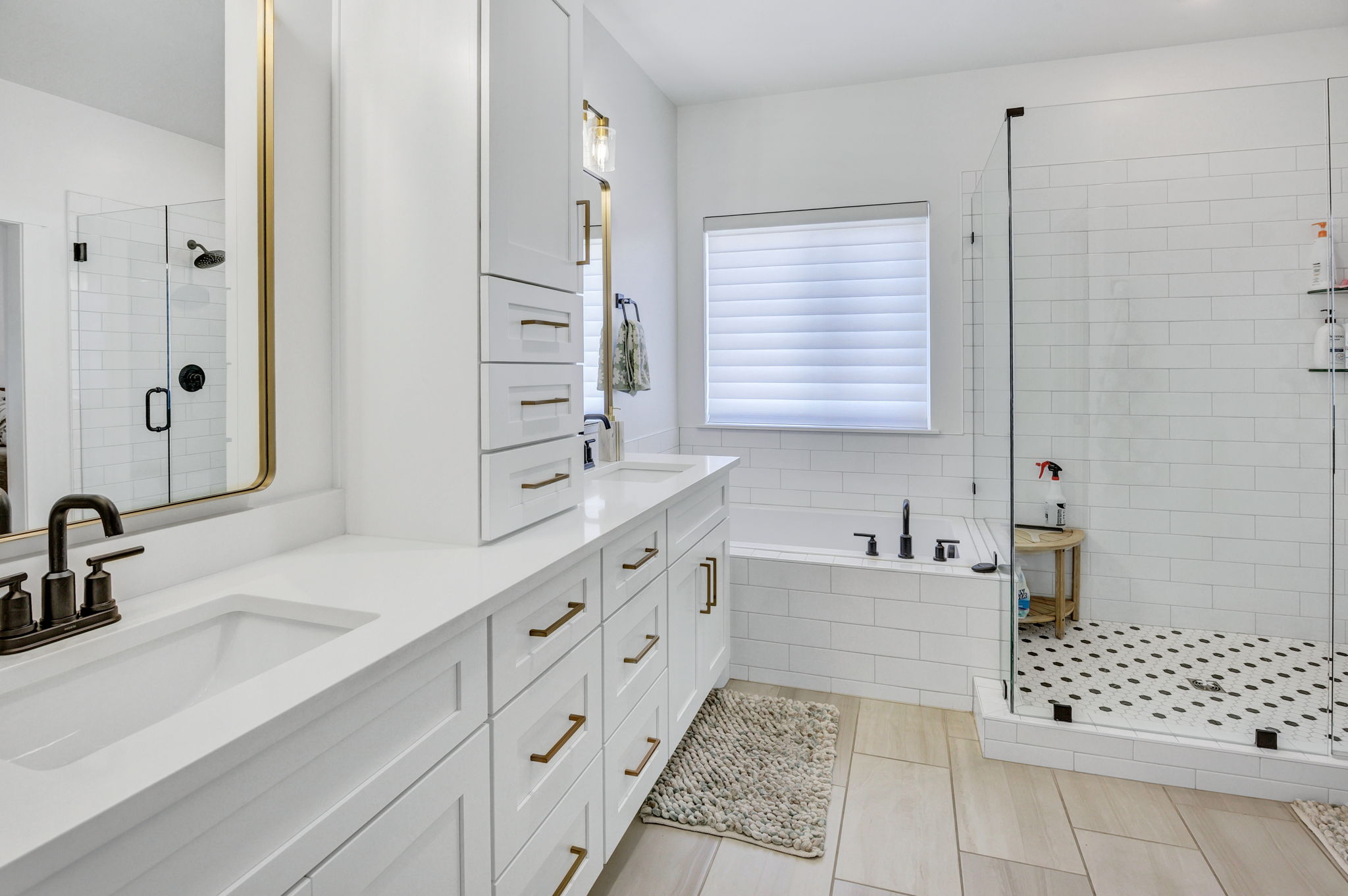 Bathroom featuring dual vanity with white cabinetry and gold-tone hardware, rectangular undermount sinks, and dark bronze fixtures
