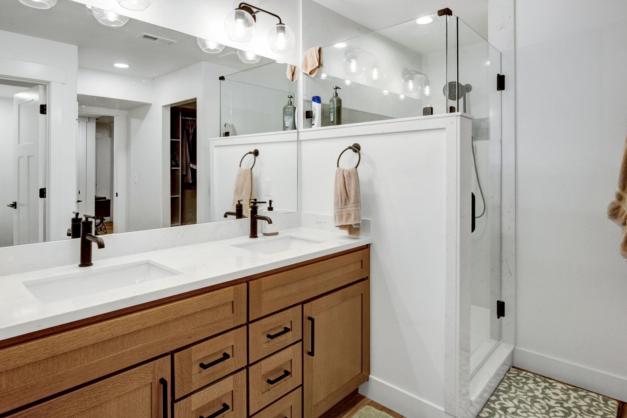 Dual-sink vanity with wood cabinetry and white countertops and large shower
