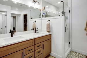 Dual-sink vanity with wood cabinetry and white countertops and large shower