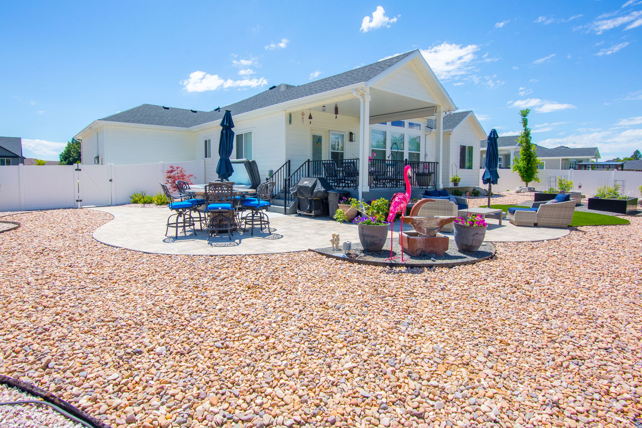 Expansive backyard featuring a large gravel area, two distinct patio spaces, a covered patio with architectural columns, and white vinyl fencing