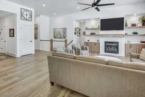 Spacious living area featuring light LVP flooring, a contemporary ceiling fan, and recessed lighting