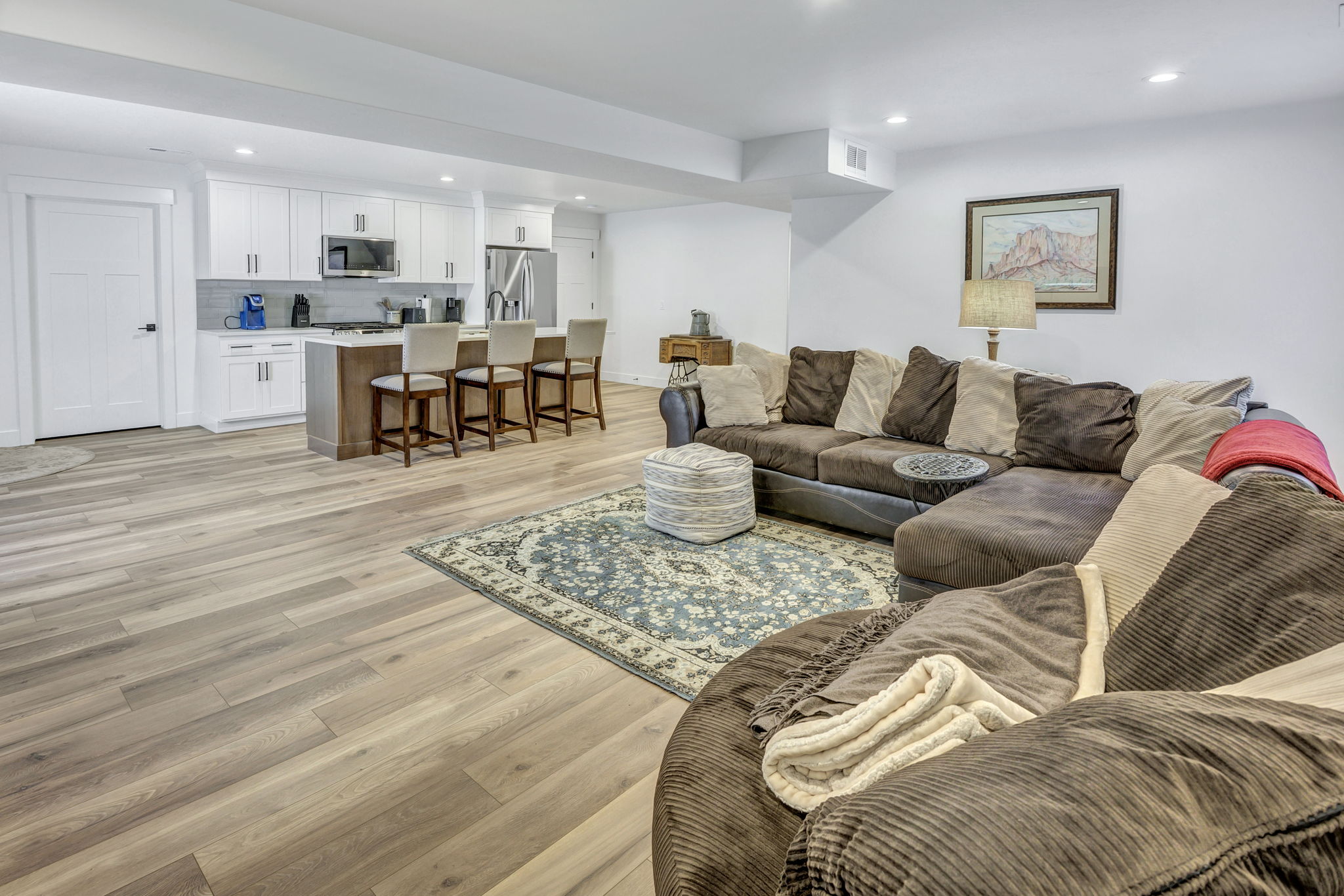 Open-concept living area featuring LVP flooring, recessed lighting, and a white kitchen with an island and stainless steel appliances