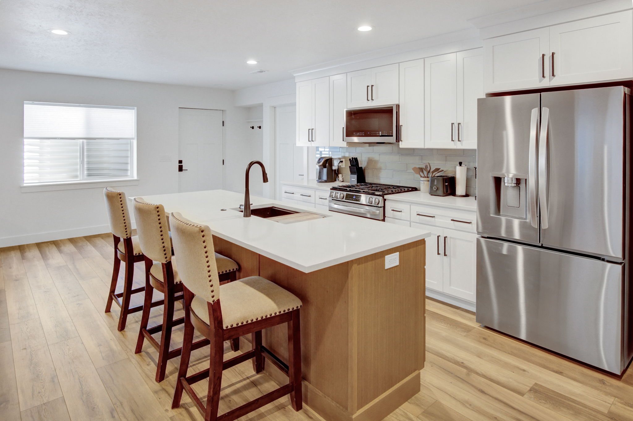 Modern kitchen in basement apartment featuring a central island with integrated sink, white cabinetry, stainless steel appliances, light LVP flooring, and a subway tile backsplash