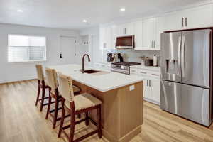 Modern kitchen in basement apartment featuring a central island with integrated sink, white cabinetry, stainless steel appliances, light LVP flooring, and a subway tile backsplash