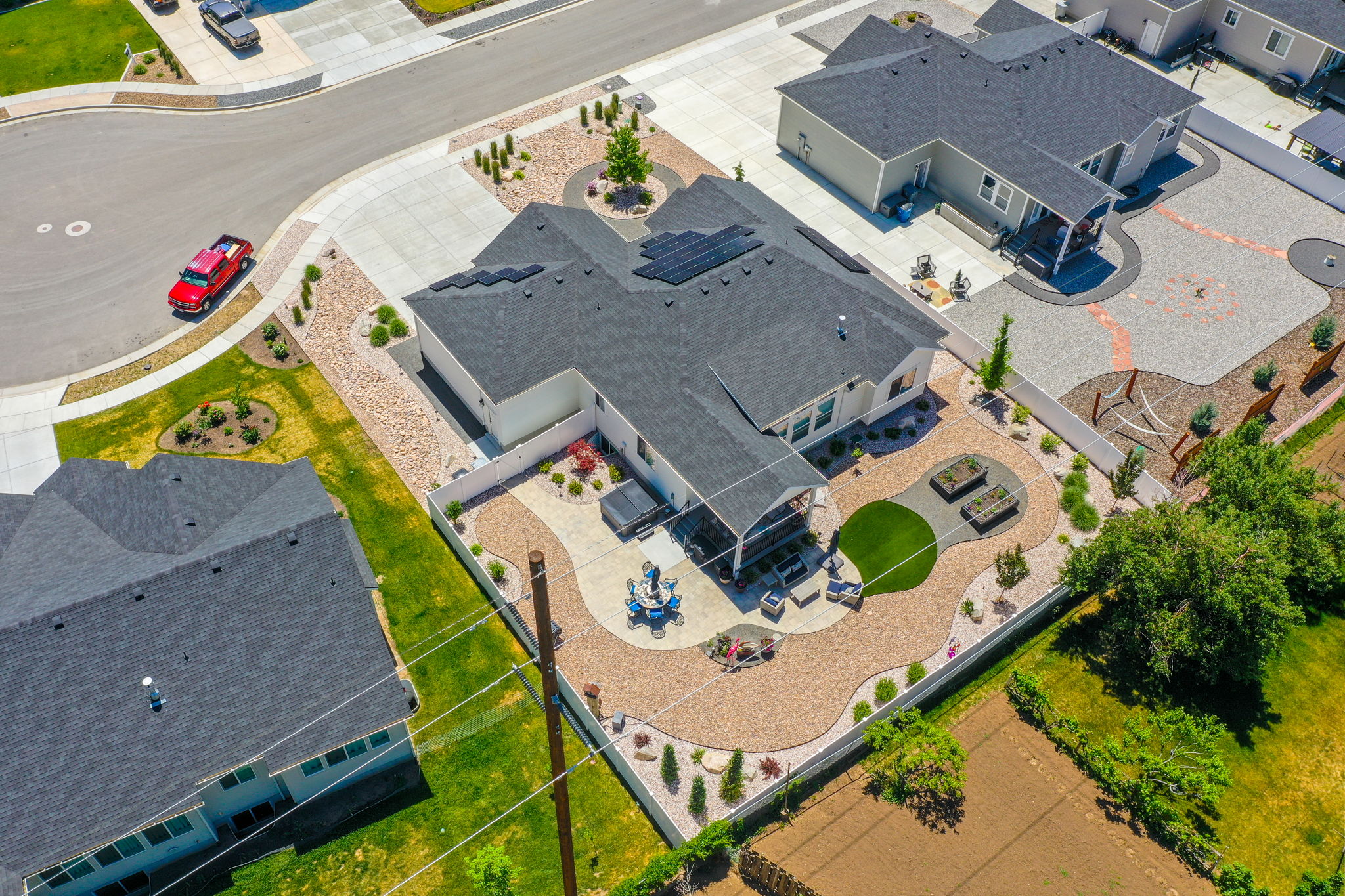 Expansive backyard featuring a covered patio, artificial turf area, two raised garden beds, and decorative gravel landscaping with mature shrubs