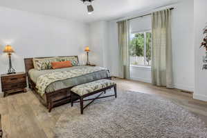 Bedroom featuring light LVP flooring, a contemporary ceiling fan, and a large window with drapes