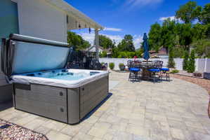 Outdoor patio featuring a lovely hot tub, paver stone hardscaping, covered patio space, and a white privacy fence