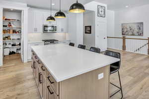 Modern kitchen featuring a large central island with quartz countertop, white cabinetry, a subway tile backsplash, stainless steel appliances, and LVP flooring