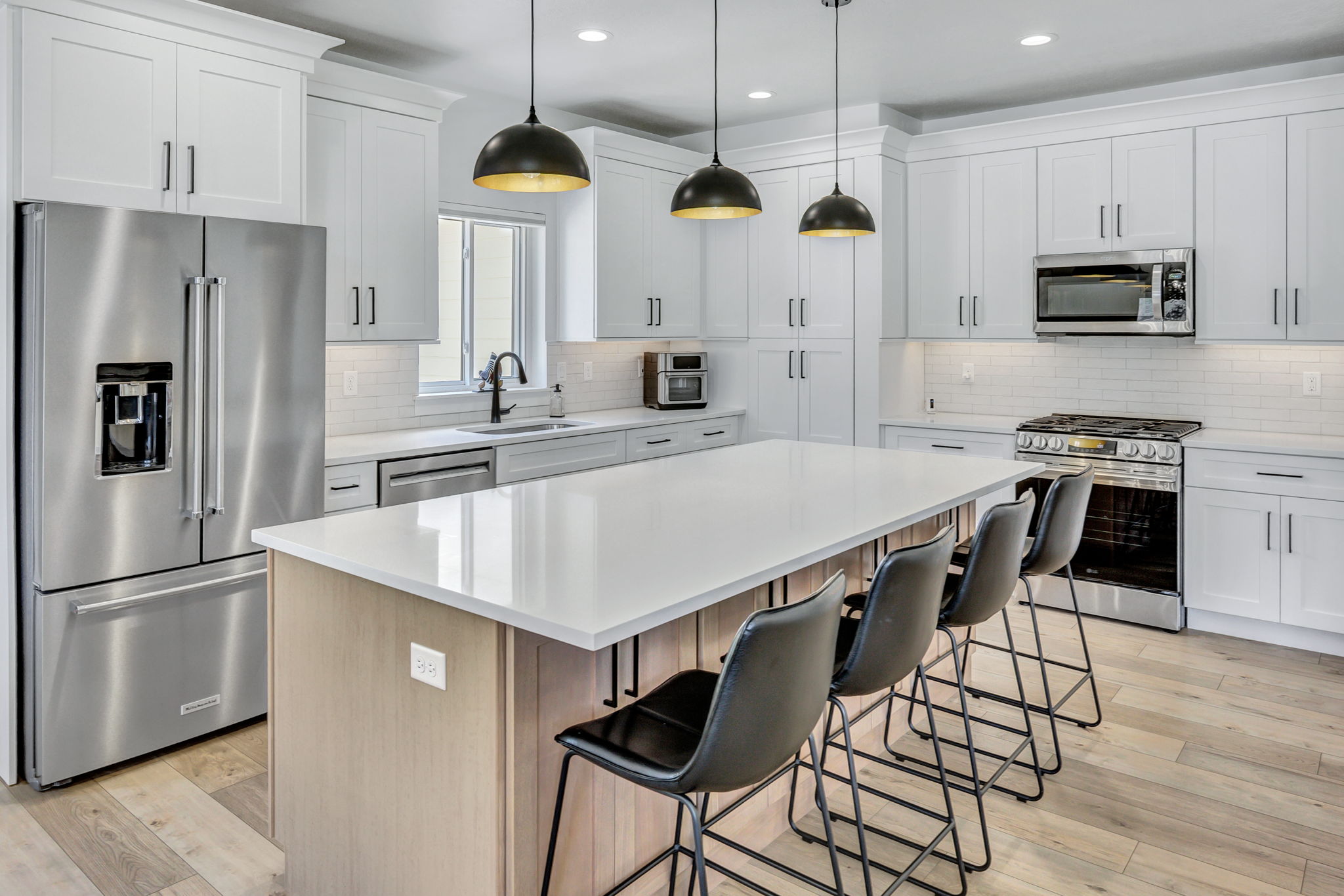 Kitchen featuring a large island with seating, stainless steel appliances, white shaker cabinetry, pendant lighting, and LVP flooring