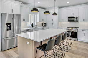 Kitchen featuring a large island with seating, stainless steel appliances, white shaker cabinetry, pendant lighting, and LVP flooring