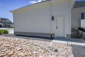 Side entry featuring a panel door with black hardware, an exterior wall lantern, and a concrete stoop