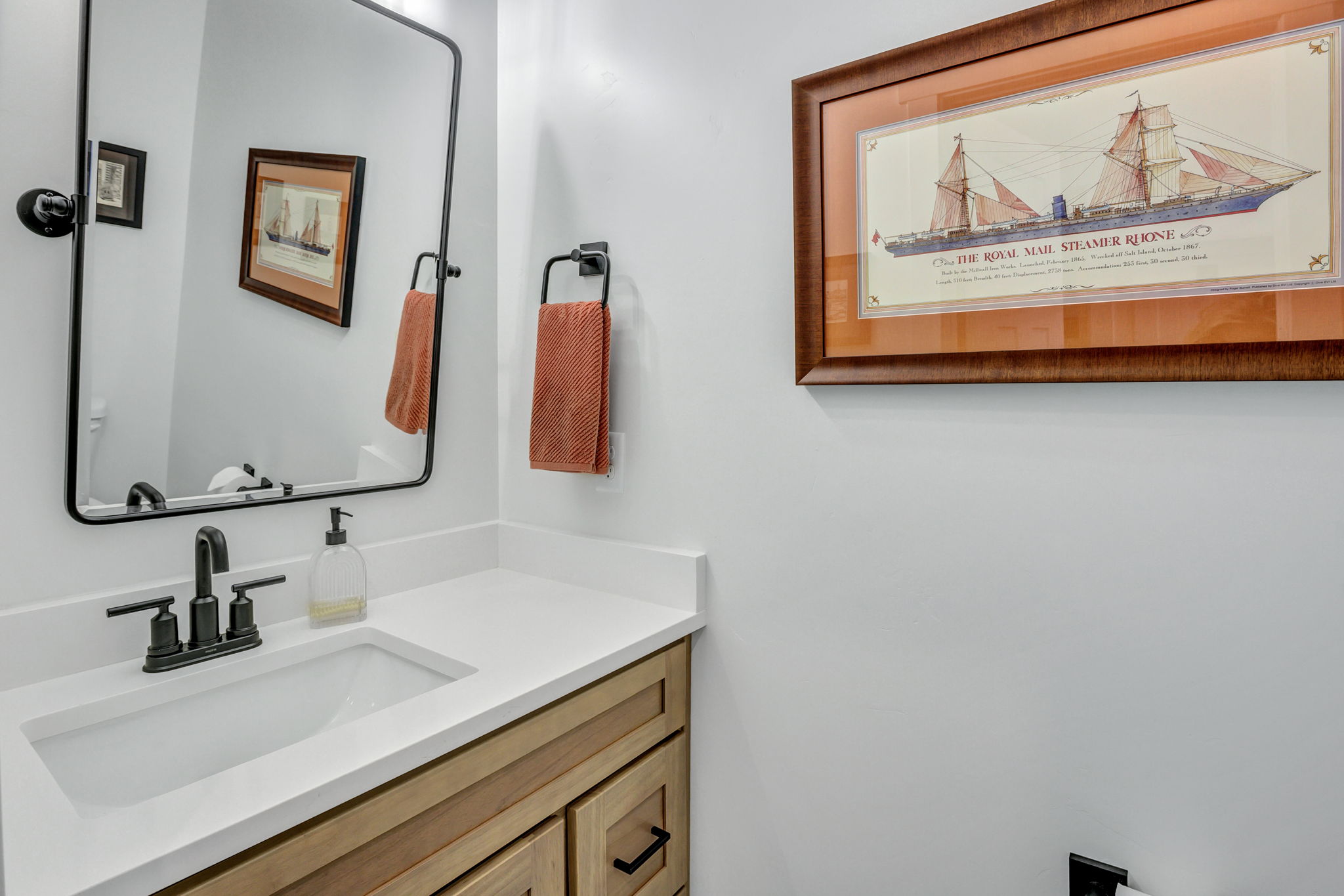 Bathroom vanity featuring a light wood-finish cabinet with black hardware, a white countertop, and an integrated rectangular sink