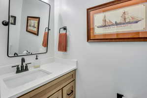 Bathroom vanity featuring a light wood-finish cabinet with black hardware, a white countertop, and an integrated rectangular sink
