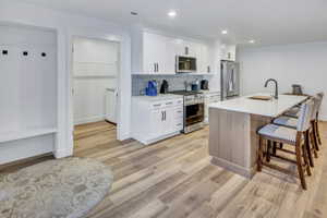 Modern kitchen featuring white cabinetry, stainless steel appliances, a white island countertop, and LVP flooring
