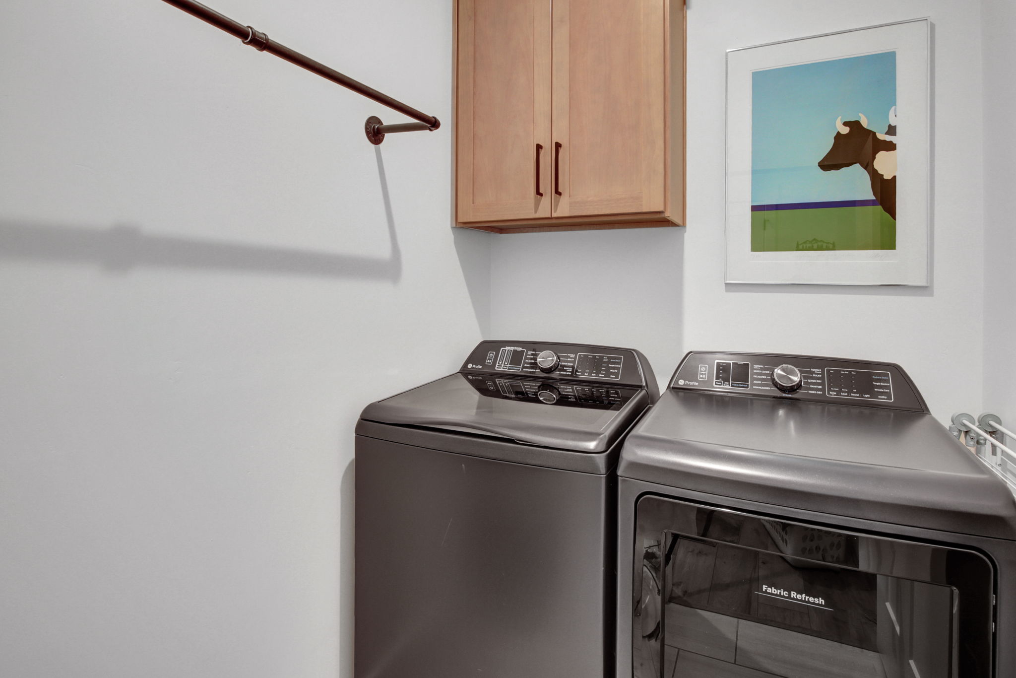 Laundry area featuring a wall-mounted drying rod and light wood-finish cabinetry