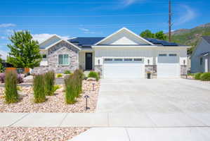 Contemporary ranch-style residence featuring a stone and board-and-batten facade, solar panels, an attached three-car garage with carriage-style doors, a concrete driveway, and low-maintenance landscaping with decorative rocks and plantings
